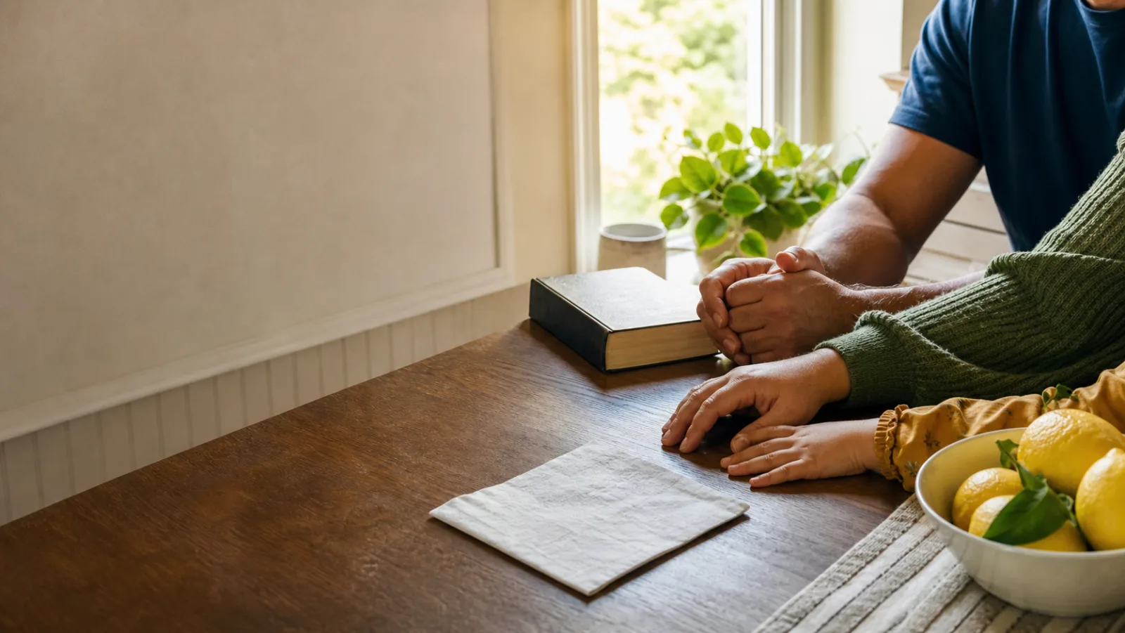 A family's hands near a Bible at a bright kitchen table