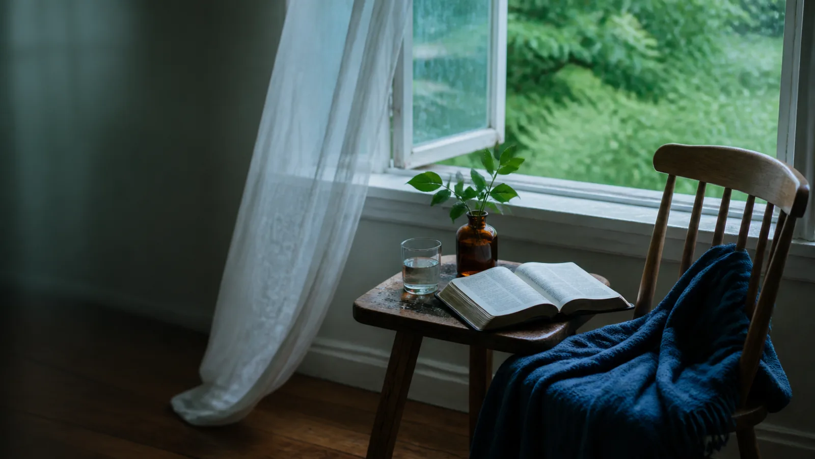 An open Bible, water, and a blue blanket beside an open window after rain